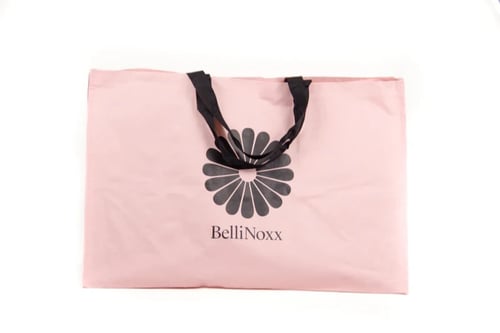 Lyserød bæretaske med sort hank og logoen "BelliNoxx" med blomstermotiv i midten. (1)