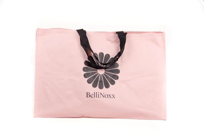 Lyserød bæretaske med sort hank og logoen "BelliNoxx" med blomstermotiv i midten.