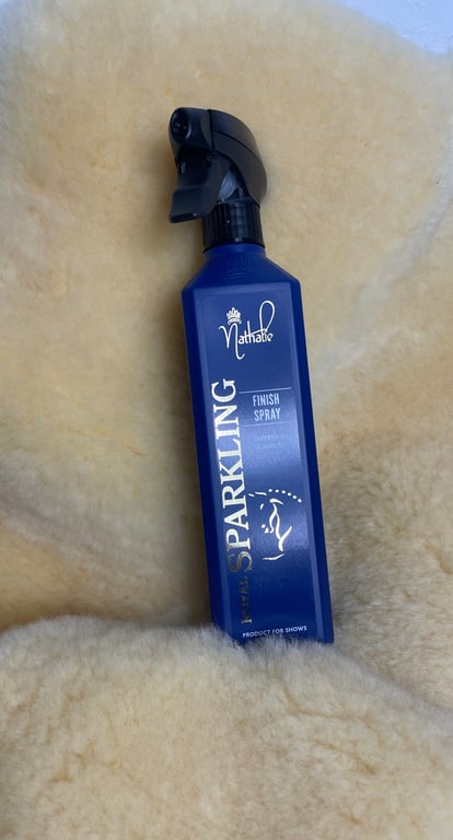 Flaske med blå finish spray fra Nathalie kaldet "Sparkling", placeret på en beige plyssoverflade.
