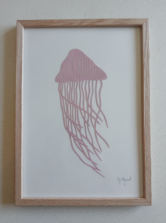 Billede af en indrammet minimalistisk kunsttegning af en lyserød vandmand på hvid baggrund med en simpel træramme.