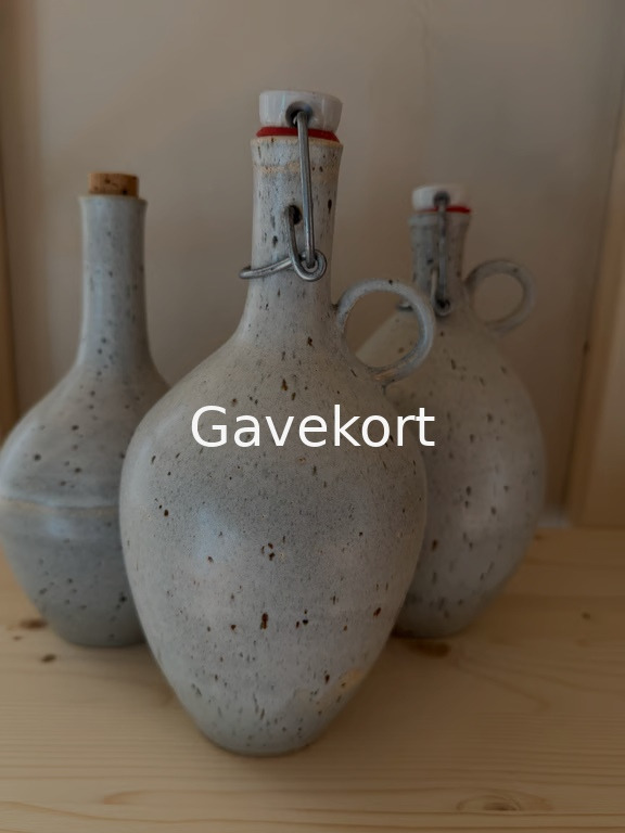 Tre grå, keramiske flasker med rustikke pletter stående på en lyse træflade, midterflasken har en porcelænslukning med metalbøjle. Tekst "Gavekort" er placeret midt på billedet.