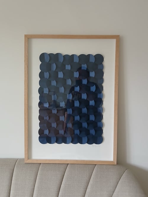 Billedramme med abstrakt kunstværk bestående af overlappende mørkeblå cirkler, hængende på en hvid væg over en beige sofa. (2)