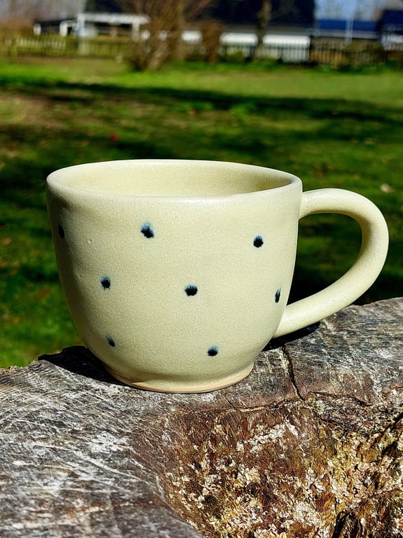 Kop med hank i mat gul glasur med sorte prikker.  