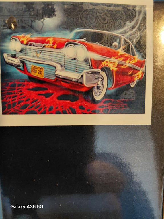 Billede af en illustration af en rød vintagebil med flammer på karrosseriet, der kører hen over en rød overflade med et mønstret baggrund.
