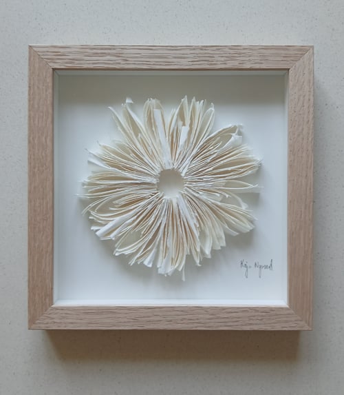 Indrammet papirkunstværk i form af en blomst lavet af foldede, flosset papirark på hvid baggrund. (3)