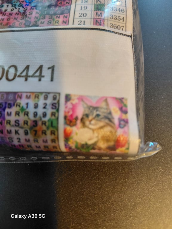 Nærbillede af et pakket diamantmaleri med en lille billedillustration af en kat omgivet af blomster.