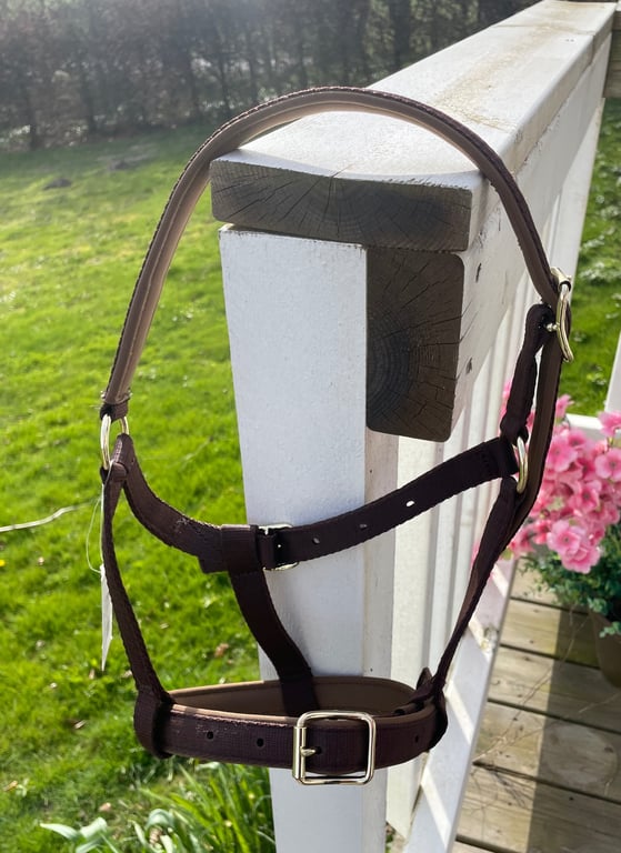 Brunt lædergrime hængende på et hvidt trægelænder med græs og blomster i baggrunden.