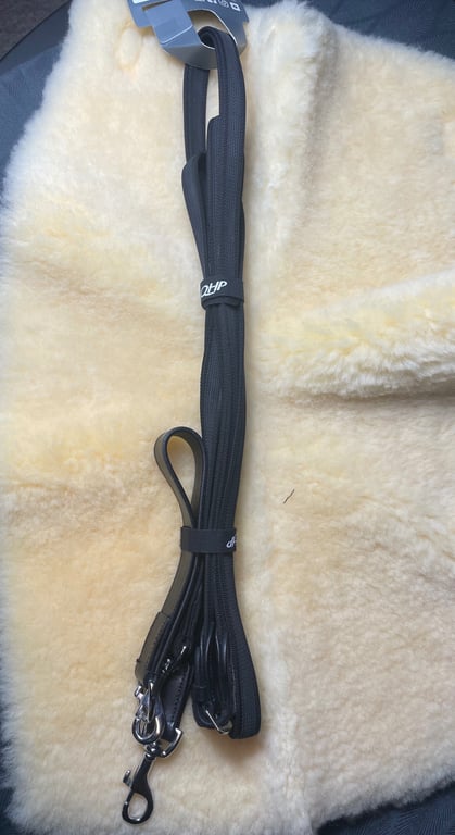 Sort hundesnor med metalclips liggende på en cremefarvet, blød uldpels.