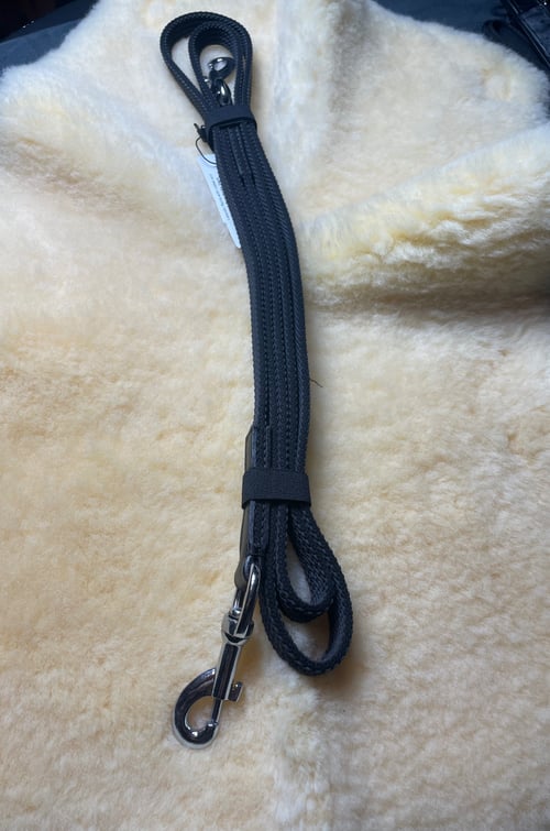 Sort flettet hundesnor med metalclip lagt på lyst plysunderlag. (1)