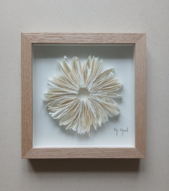 Indrammet kunstværk bestående af albummet sider foldet radielt ud, der danner en cirkulær blomst-lignende form, med en lys træramme.