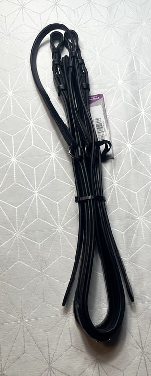 Sort læder hundesnor med metalclips, lagt sammen på hvidt mønstret underlag.