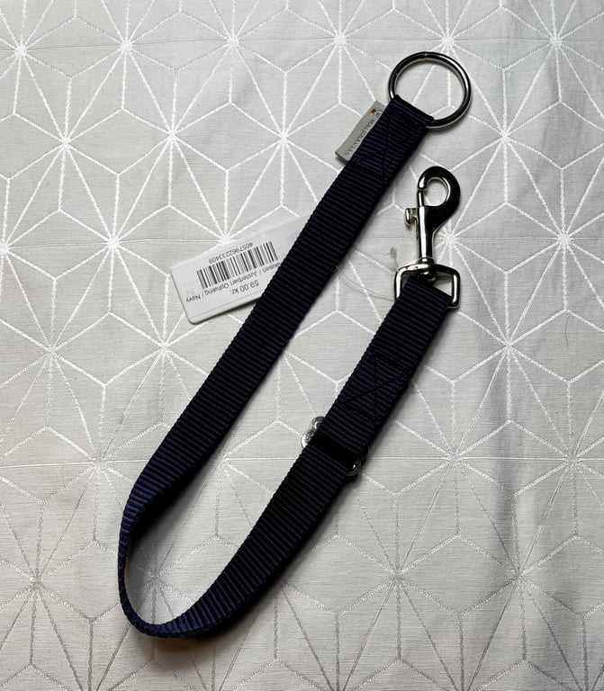 Sort justerbar hundesnor med metalring i den ene ende og karabinhage i den anden, placeret på et mønstret, lyst underlag.
