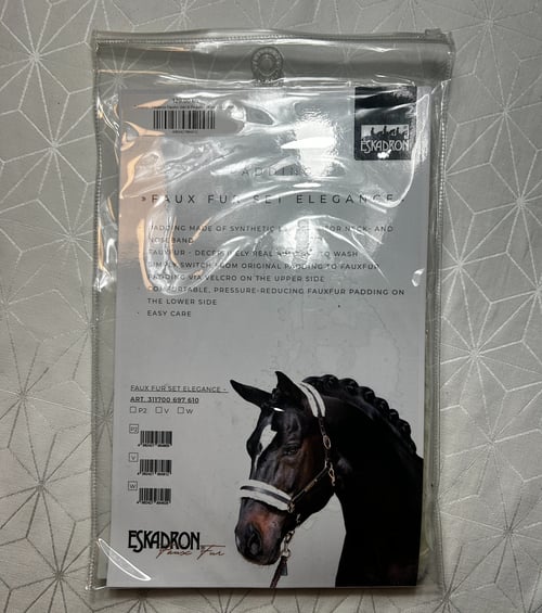 Transparent plastikpose med emballage til Eskadron Faux Fur Set Elegance, hvor der ses et billede af en sort hest med flettet man og hvidt hovedtøj med syntetisk pelsindlæg. (1)
