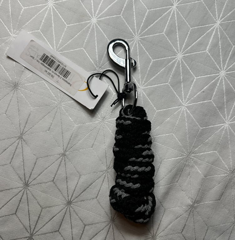 Sort og gråt flettet reb med metal karabinhage og prismærke lagt på gråt mønstret stof.