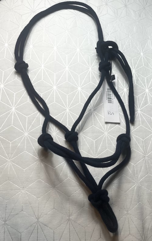 Sort rebshalsbånd med knuder lagt ud på mønstret, lyst underlag med geometrisk design. (1)