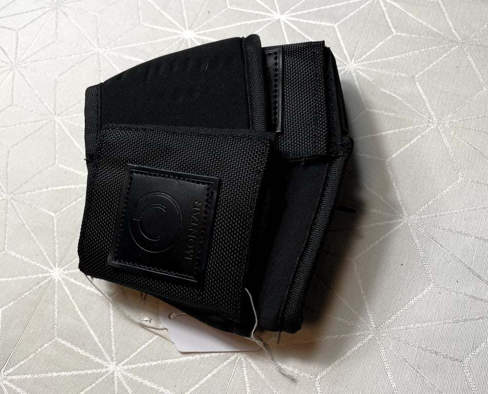 Sort velcro-omslag med mærket "Montar" lagt på et lyst tekstil med geometrisk mønster.