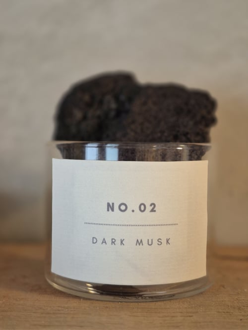 Et klart glas med et label, hvor der står "No.02 Dark Musk", og mørke, skumpede genstande inde i glasset. (1)