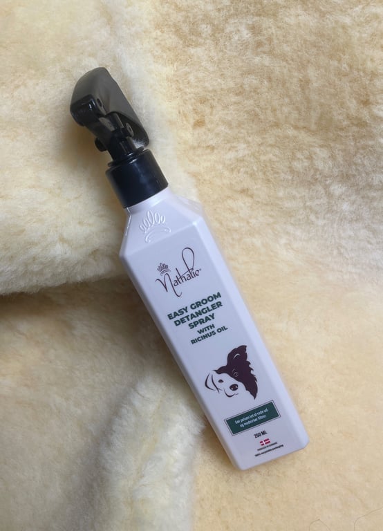 Flaske med Nathalie Easy Groom Decangler Spray til hunde, placeret på beige uldagtigt stof.