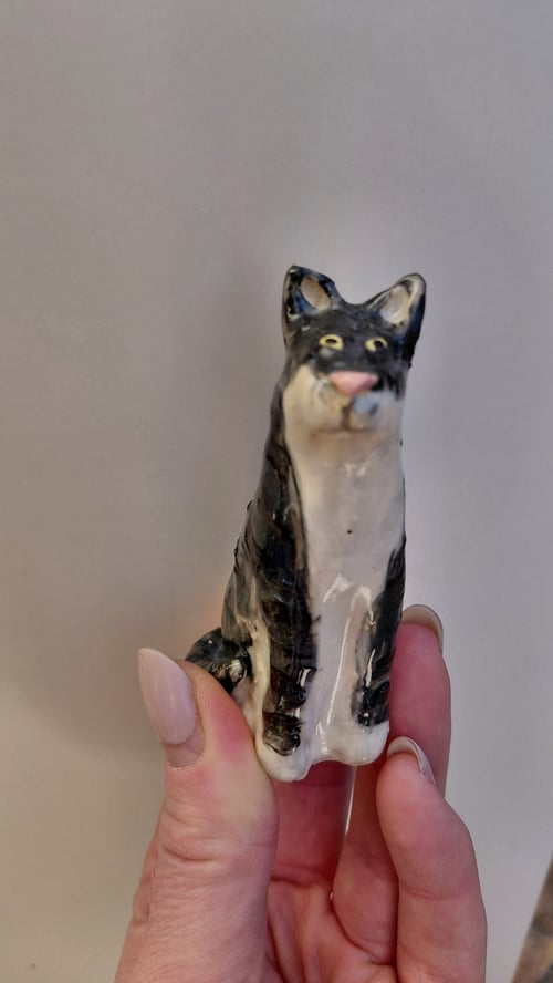 Hånd, der holder en lille keramisk figur af en sort-hvid kat. (1)