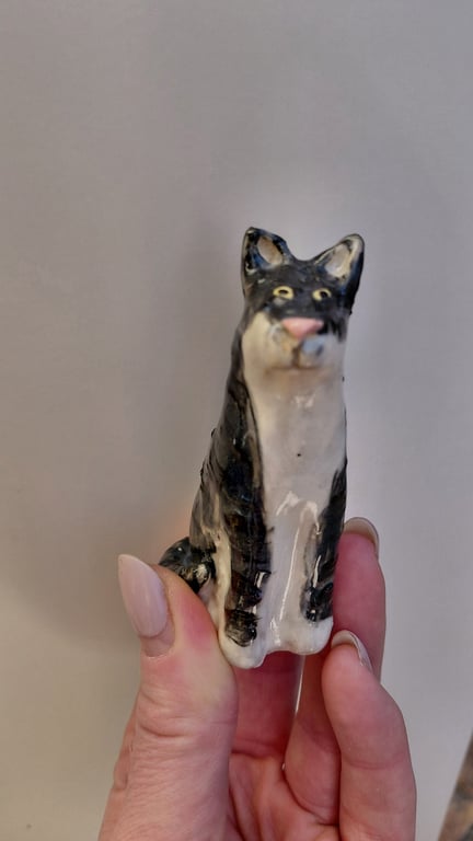 Hånd, der holder en lille keramisk figur af en sort-hvid kat.