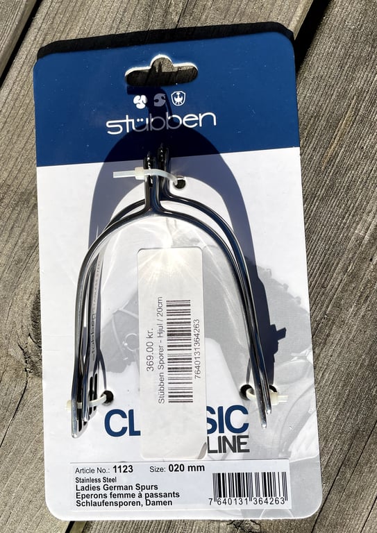 Stübben klassiske stålsporer til damer i størrelse 20 mm, pakket på blå og hvid emballage, liggende på træoverflade.