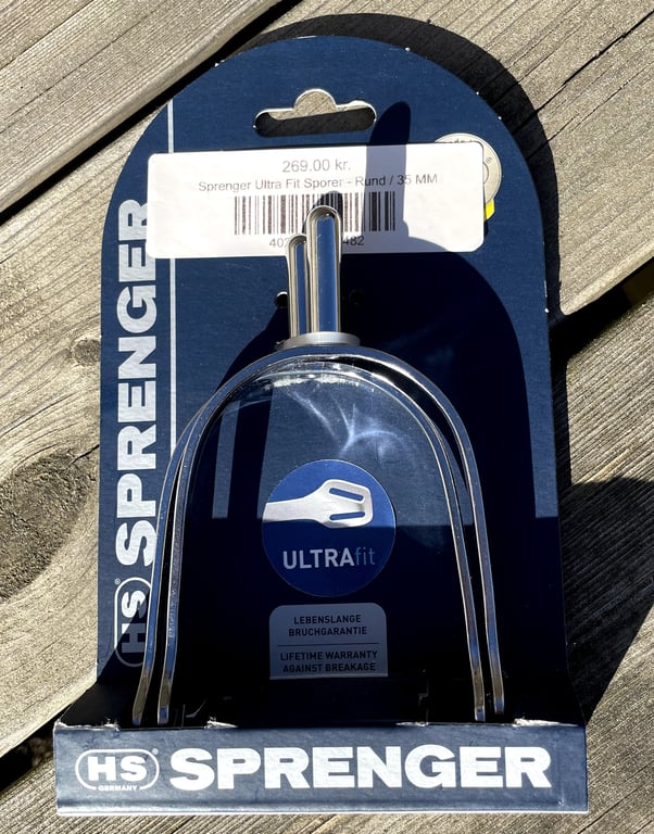 Billede af en HS Sprenger Ultra Fit spore i rund 35 mm, med emballage og prislabel på 269,00 kr., placeret på træoverflade.