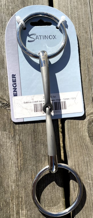 Billede af en Satinox 2-delt bid med løse ringe i metal på original emballage, lagt på træbord.