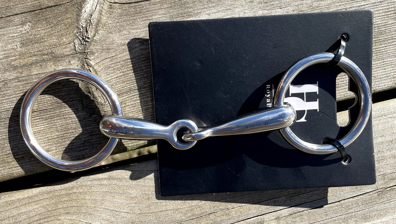Ridestang af metal med to store ringe på hver ende, lagt på en sort papplade og placeret på et træbord.