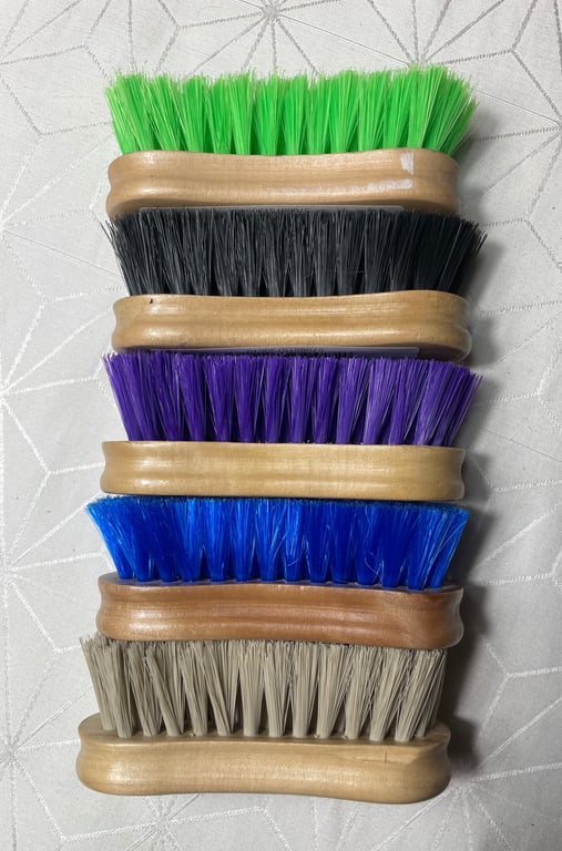 Fem rækker rengøringsbørster med forskellige farvede børster (grøn, sort, lilla, blå og beige) med træskaft stablet ovenpå hinanden.
