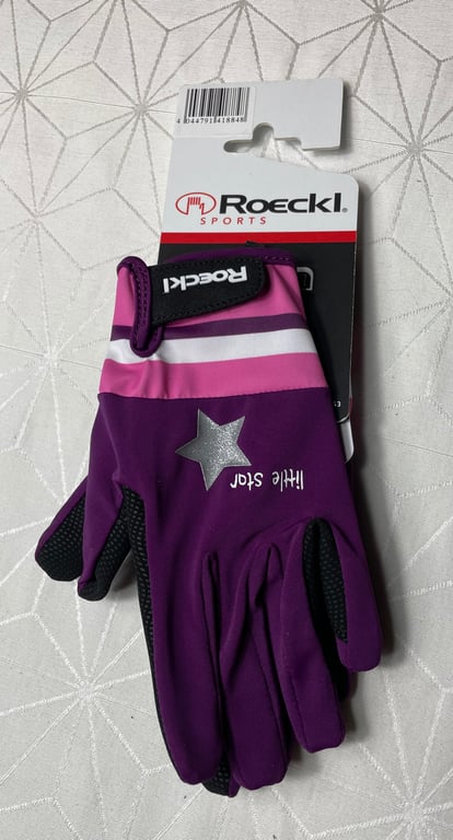 Lilla og pink Roeckl sports handsker med teksten "little star" og en sølvstjerne, lagt på en hvid overflade med mønster.
