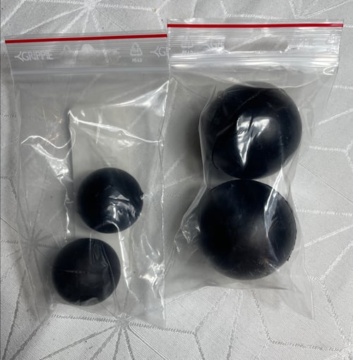 To plastikposer indeholdende to sorte bolde hver, placeret på en hvid overflade med mønster. (1)