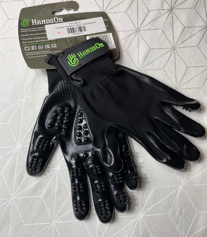 Sort HandsOn-hundegroominghandske med knopper til pelspleje, ligger på lyst mønstret underlag.