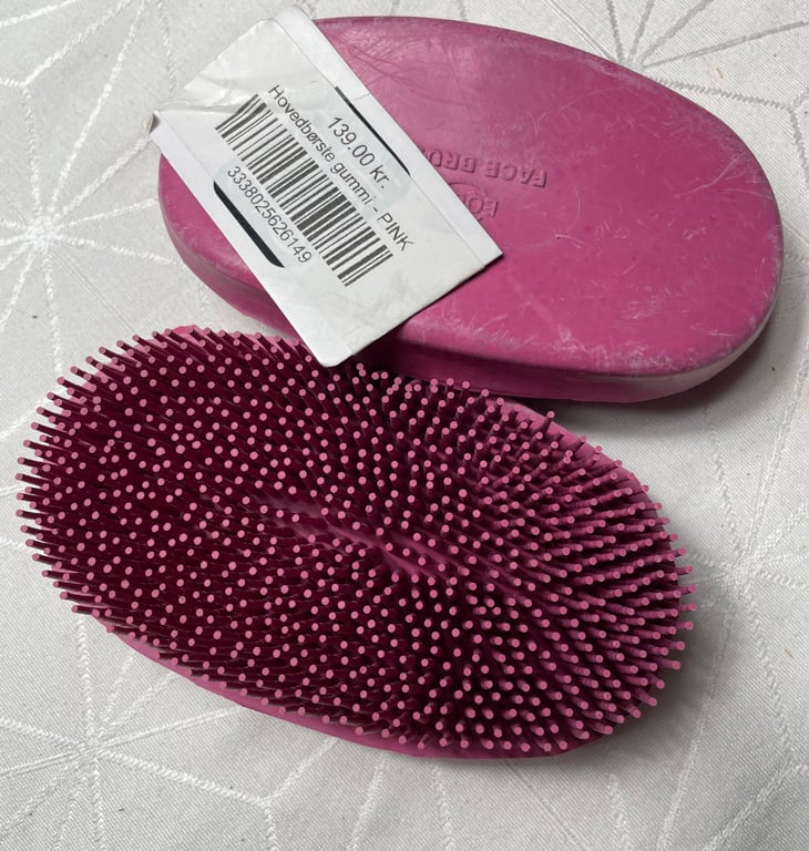 Pink hovedbørste i gummi med fine børstehår, lagt på hvidt stof med prisetiket på 139,00 kr.