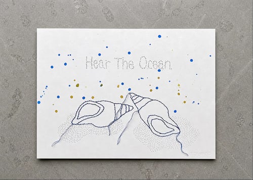 Et hvidt lærred med broderi af to blå muslinger og teksten "Hear The Ocean" øverst. Der er blå og gule farvepletter spredt over lærredet, og nederst til højre står ordet "TIDEVAND". (1)