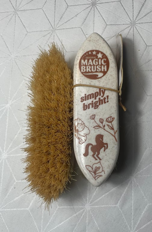 Billedet viser en Magic Brush neglebørste med beige børstehår og et hvidt håndtag med brun tekst og illustrationer, herunder en hest og blomster.