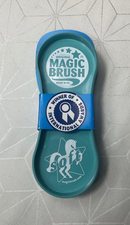 Børste i plastik med mærkat "Original Magic Brush", "Winner of International Awards" og "Soft" på en lysegrå baggrund.
