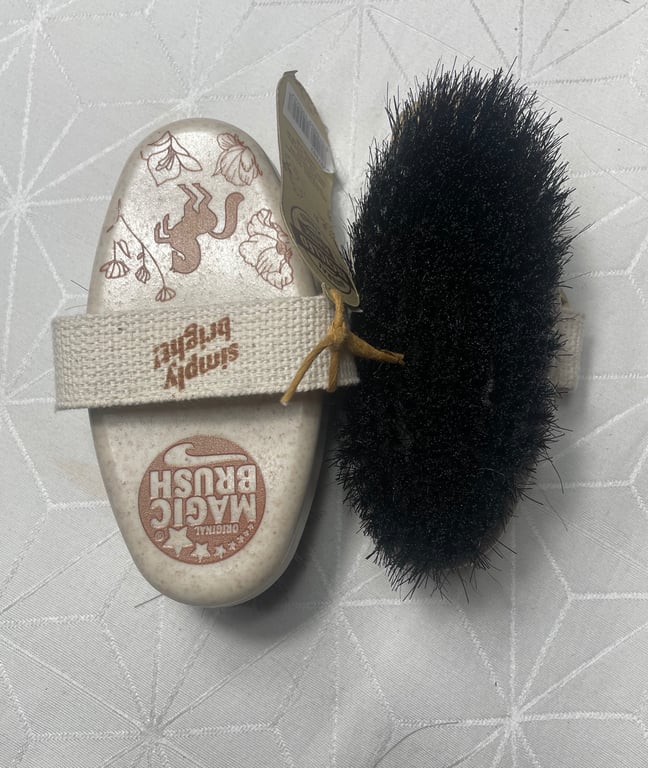 Børste med sorte hår og hvidt håndtag med strop og tekst "Magic Brush" og "Simply Bristle" på.