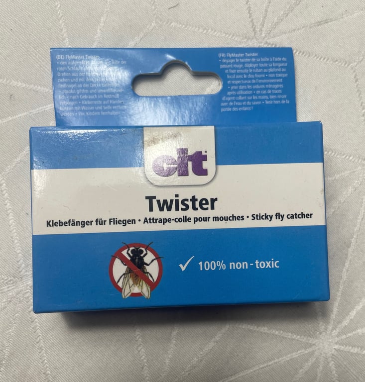 Pakke med blå og hvid etikette til "cit Twister", en klistret fluefanger, mærket som 100% ikke-giftig, med tekst på tysk, fransk og engelsk.
