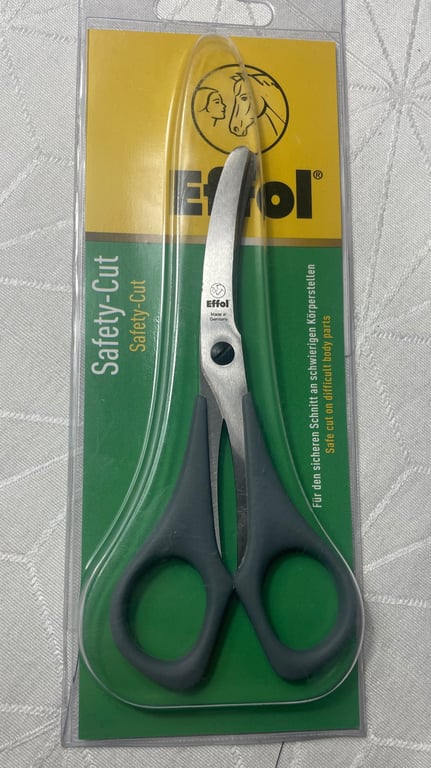 Saks med buede blade i original emballage, mærket Effol Safety-Cut til sikker klipning af vanskelige kropsdele, med grå håndtag og gul-grøn baggrund.