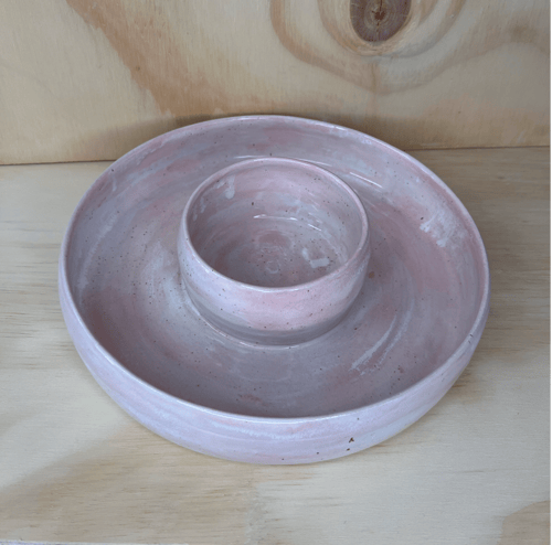 Pink keramisk dipfad med en rund skål i midten, placeret på et lyst træbord. (1)