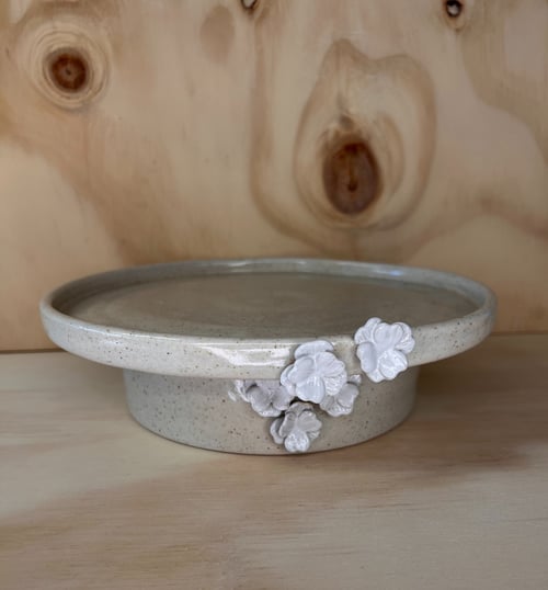 Keramisk kagefad med beige glasur og små hvide blomsterdekorationer, placeret på lyst træbord med træbaggrund. (1)