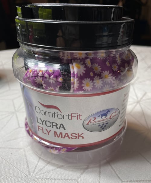 Transparent plastbeholder med sort låg indeholdende en lilla flyvemaske med hvid-gule blomster, mærket "ComfortFit Lycra Fly Mask" fra Professional's Choice. (1)
