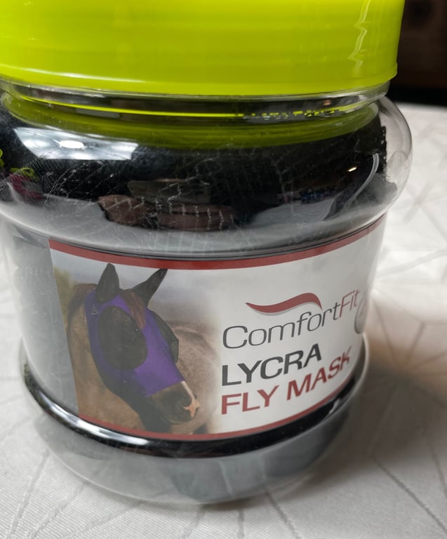 Gennemsigtig plastikbeholder med en lyserød hætte, der indeholder en sort Lycra fluemaske til heste med mærket ComfortFit.