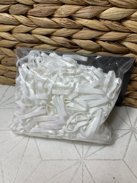 Plastpose med mange hvide elastikker foran en flettet kurv.