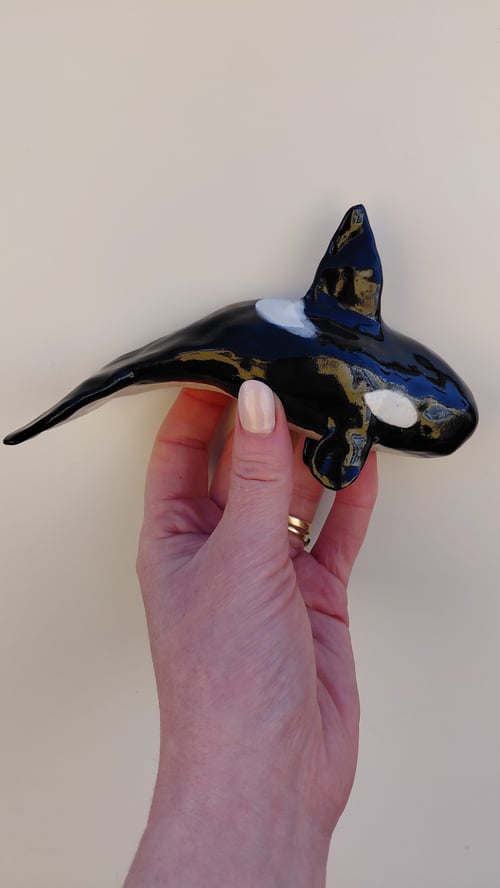 Hånd, der holder en sort og hvid keramisk figur af en spækhugger. (1)