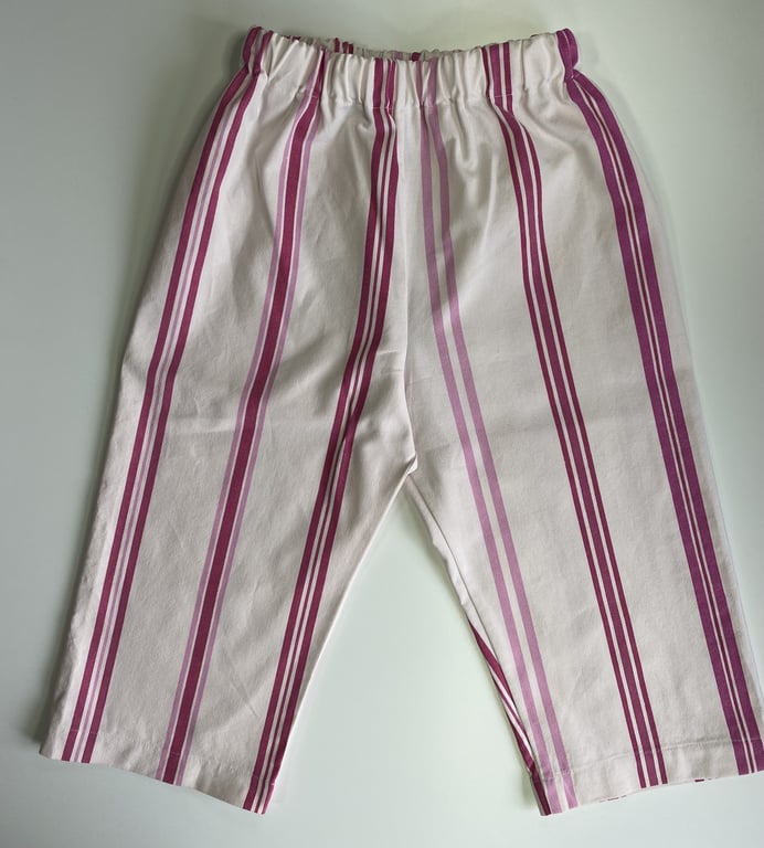 Børnebukser med elastisk talje og lodrette pink og lilla striber på hvid baggrund.