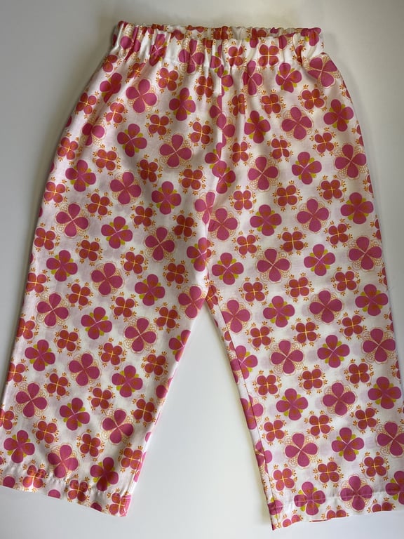 Bukser til børn med elastik i taljen og mønster af pink og orange blomster på hvid baggrund.