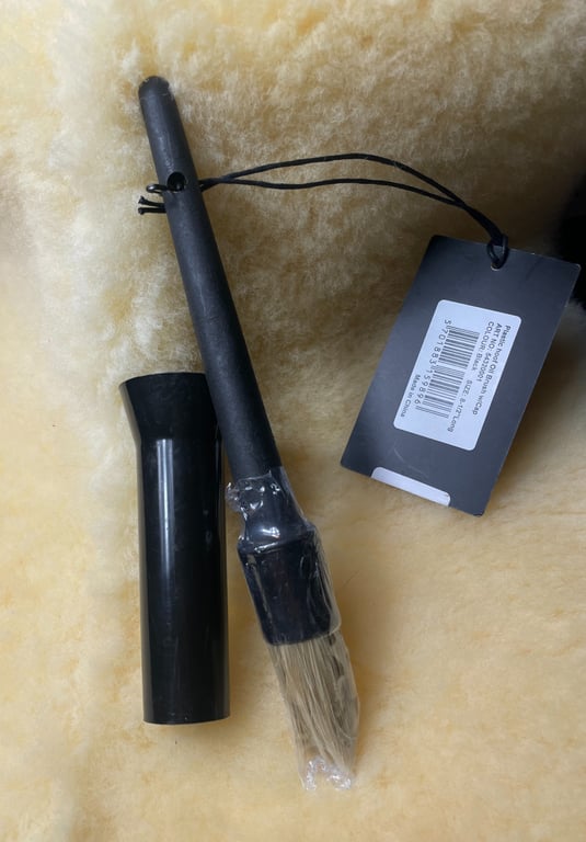 Sort pensel med plastikbeskyttelse og sort hætte liggende på lyst uldmateriale med pris- og stregkodeetiket fastgjort.