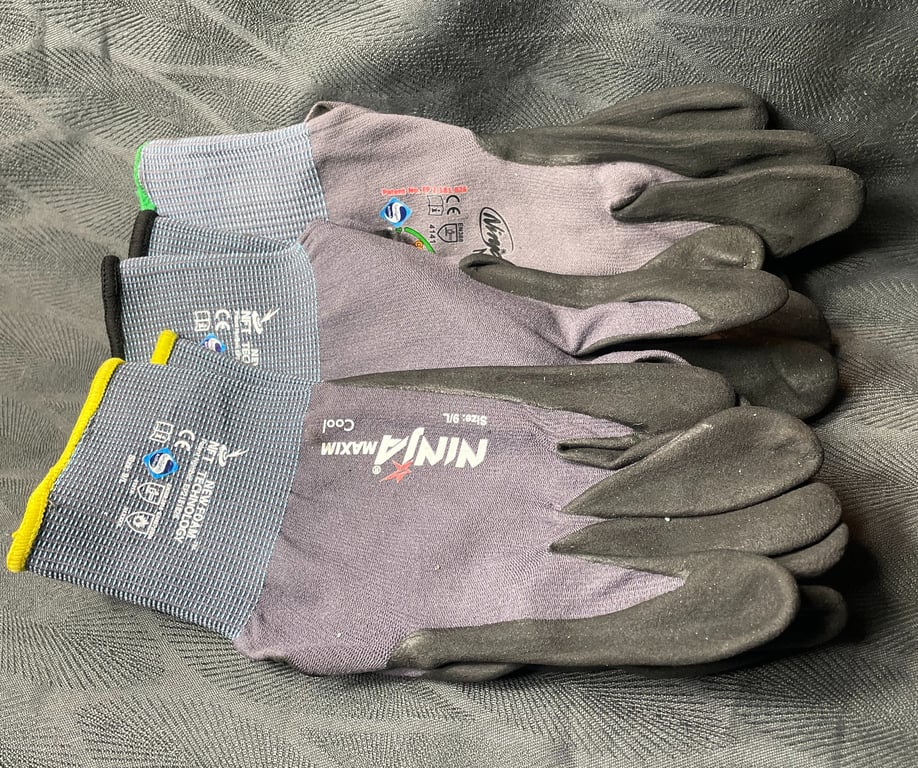 To arbejdshandsker af mærket NINJA MAXIM og NINJA COOL, lagt oven på hinanden på en mørk tekstilbaggrund.