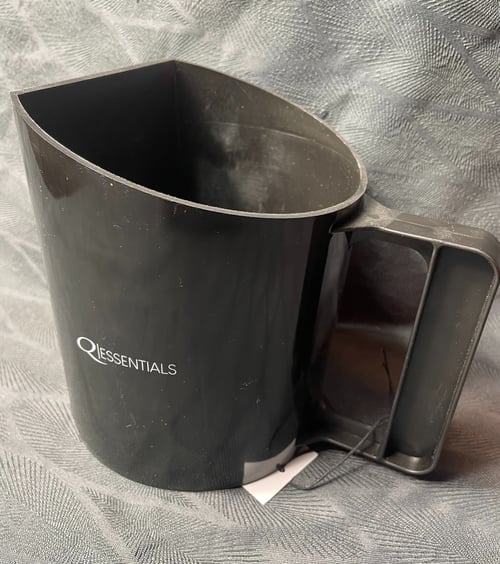 Sort plastik mælkeskummer med mærket "QI ESSENTIALS" på siden, placeret på en grå tekstureret overflade. (1)